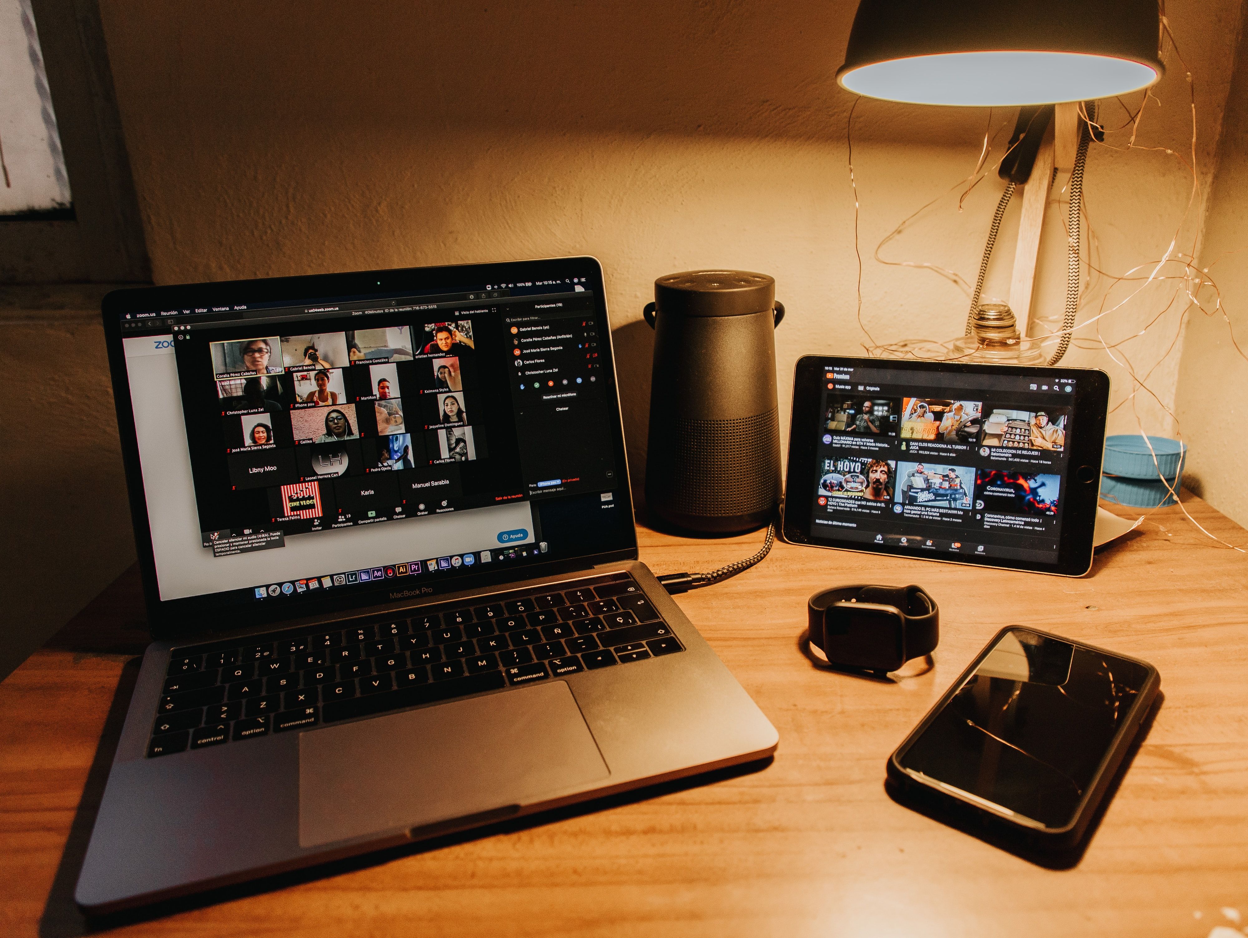 A Zoom meeting on a laptop and a tablet next to a smart watch and mobile phone